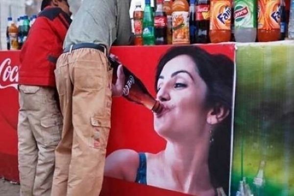 Мужик стоит возле плаката с девушкой пьющей из горла бутылки